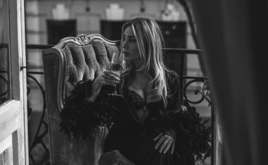 Peignoir giymiş bir kadın ve bir kadeh şarap. Tüylü siyah ipek bornozlu Avrupalı sarışın kadının şehvetli fotoğrafı. Moda konsepti