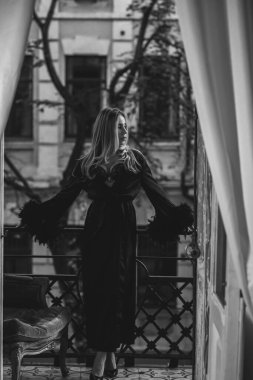 Peignoir giymiş bir kadın ve bir kadeh şarap. Tüylü siyah ipek bornozlu Avrupalı sarışın kadının şehvetli fotoğrafı. Moda konsepti