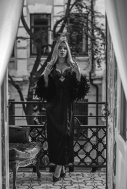 Peignoir giymiş bir kadın ve bir kadeh şarap. Tüylü siyah ipek bornozlu Avrupalı sarışın kadının şehvetli fotoğrafı. Moda konsepti
