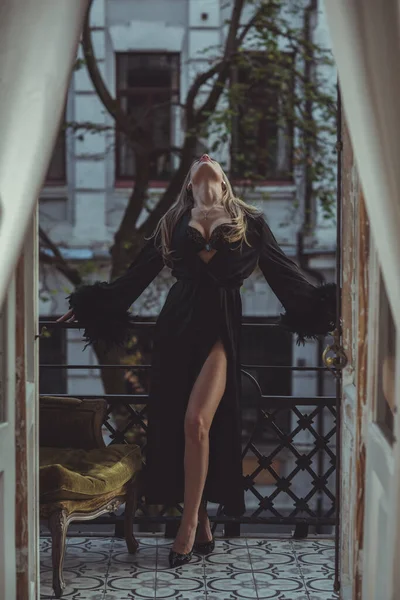 女士在皮斯诺 喝一杯葡萄酒 欧洲金发女人穿着带羽毛袖子的黑色丝绸长袍的性感照片 时尚的概念 免版税图库照片