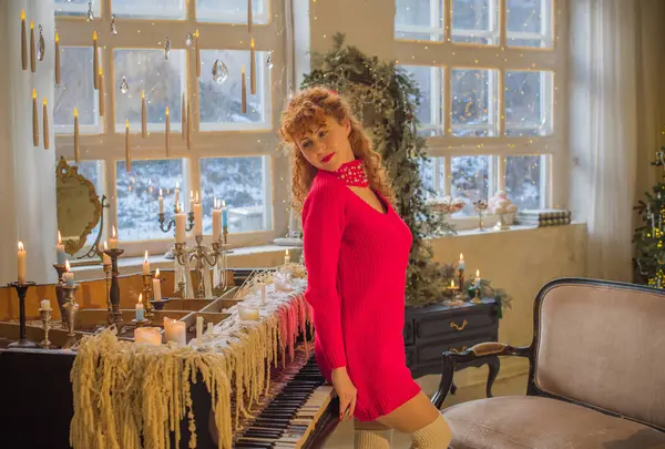 Warm cozy home scene, vintage Scandinavian style. Young redhead curly woman in red sweater celebrating winter, happy moments of life
