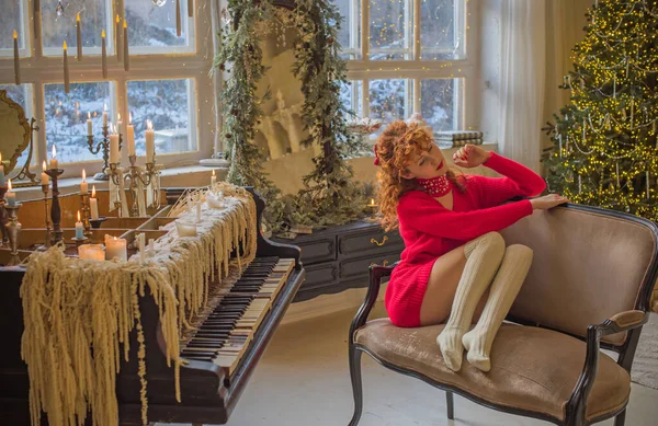 Warm cozy home scene, vintage Scandinavian style. Young redhead curly woman in red sweater celebrating winter, happy moments of life