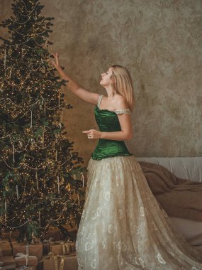 Tatil günlerindeki sarışın güzel bayan Noel atmosferi, parti havası. Yeşil ve bej elementli süslü elbiseli genç bayan. 