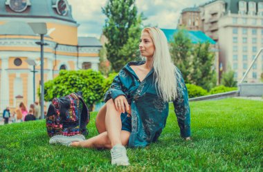 Genç Avrupalı sarışın kız şehir parkındaki çimlerin üzerinde yorucu bir günün ardından dinleniyor. Gençlik psikolojisi kavramı