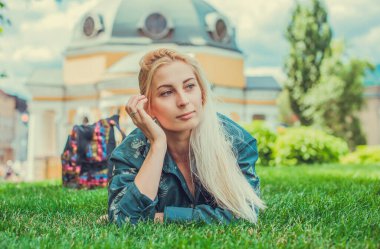 Genç Avrupalı sarışın kız şehir parkındaki çimlerin üzerinde yorucu bir günün ardından dinleniyor. Gençlik psikolojisi kavramı