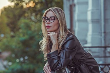 Bahar - Sonbahar koleksiyonu. Şehrin arka planında deri ceketli sarışın bir kadın. Modern klasik kadın kıyafetleri.