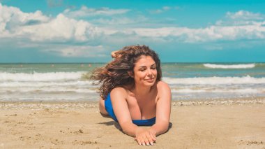 Sahilde gevşeyen kıvırcık saçlı İspanyol orta yaşlı kadın. Doğal kadın güzelliği, kadınsı konsept.