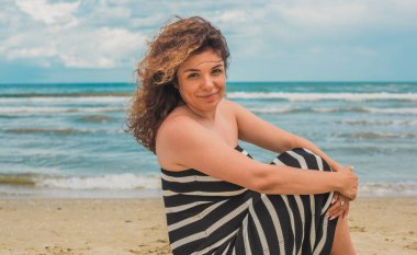 Sahilde gevşeyen kıvırcık saçlı İspanyol orta yaşlı kadın. Doğal kadın güzelliği, kadınsı konsept.