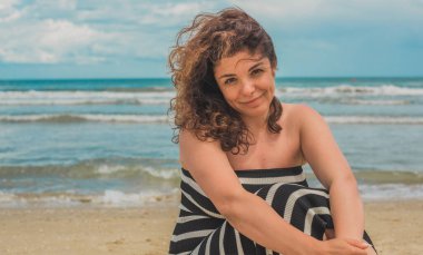 Sahilde gevşeyen kıvırcık saçlı İspanyol orta yaşlı kadın. Doğal kadın güzelliği, kadınsı konsept.