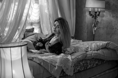 Klasik Fransız atmosferinde Peignoir giymiş bir kadın. Tüylü siyah ipek bornozlu Avrupalı sarışın kadının şehvetli fotoğrafı. Moda konsepti