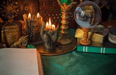 Parlayan mumların, antik tarot kartlarının, kristal kürenin ve sihirli ayin aletlerinin yer aldığı güzel düzenlenmiş bir cadı sunağı sahnesi. Bu atmosferik bileşim mistik enerjinin, ruhani uygulamanın ve esrarengiz zarafetin özünü çağrıştırıyor.