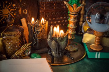 Parlayan mumların, antik tarot kartlarının, kristal kürenin ve sihirli ayin aletlerinin yer aldığı güzel düzenlenmiş bir cadı sunağı sahnesi. Bu atmosferik bileşim mistik enerjinin, ruhani uygulamanın ve esrarengiz zarafetin özünü çağrıştırıyor.