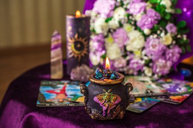 Mor bir buketi, parlak mumları, iyileştirici kristalleri ve mor bir masaya yerleştirilmiş şık gözlükleri olan mistik düz bir yatak. Kompozisyon, gizemli bir yaşam tarzını, ruhani farkındalığı ve sessiz ayinlerin sihrini yansıtıyor..  