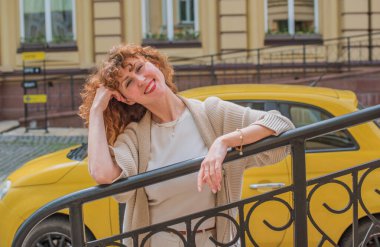 Şehirde gülümseyen kızıl saçlı kadın. Samimi anlar. 30 'lu yaşlarının sonunda ya da 40' lı yaşlarının başında bir bayan, şehir ortamında samimi bir şekilde gülümsüyor.