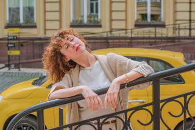 Zarif, olgun, kızıl saçlı, beyaz elbiseli, güzel Avrupalı bir kadın. Şehir Caddesinde Şehir Yürüyüşü 'nün tadını çıkarıyor.