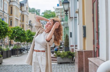 Zarif, olgun, kızıl saçlı, beyaz elbiseli, güzel Avrupalı bir kadın. Şehir Caddesinde Şehir Yürüyüşü 'nün tadını çıkarıyor.