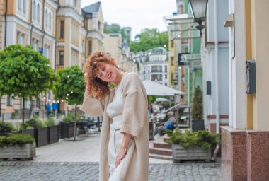 Zarif, olgun, kızıl saçlı, beyaz elbiseli, güzel Avrupalı bir kadın. Şehir Caddesinde Şehir Yürüyüşü 'nün tadını çıkarıyor.