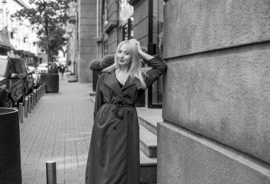 Gri ceketli olgun Avrupalı sarışın kadın şehir merkezinde yürüyor, modaya uygun trendler.