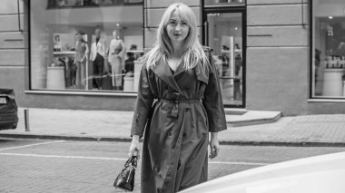 Gri ceketli olgun Avrupalı sarışın kadın şehir merkezinde yürüyor, modaya uygun trendler.