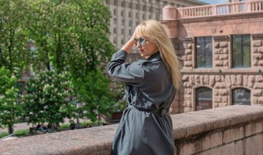 Gri ceketli olgun Avrupalı sarışın kadın şehir merkezinde yürüyor, modaya uygun trendler.