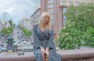 Gri ceketli olgun Avrupalı sarışın kadın şehir merkezinde yürüyor, modaya uygun trendler.