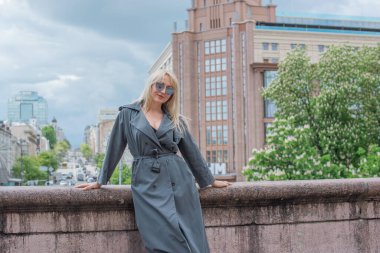 Gri ceketli olgun Avrupalı sarışın kadın şehir merkezinde yürüyor, modaya uygun trendler.