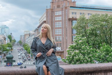 Gri ceketli olgun Avrupalı sarışın kadın şehir merkezinde yürüyor, modaya uygun trendler.