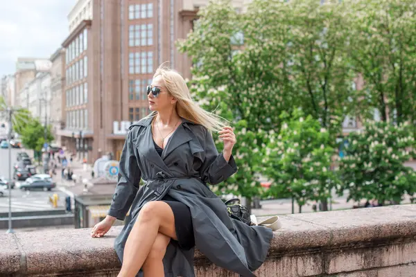 Gri ceketli olgun Avrupalı sarışın kadın şehir merkezinde yürüyor, modaya uygun trendler.