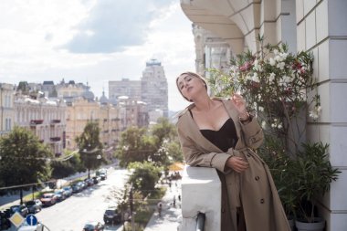 Bej ceketli, çoraplı ve siyah iç çamaşırlı bir kadın. Avrupalı sarışının balkondaki şehvetli fotoğrafı..