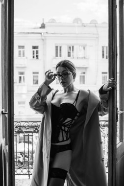 Bej ceketli, çoraplı ve siyah iç çamaşırlı bir kadın. Avrupalı sarışının balkondaki şehvetli fotoğrafı..