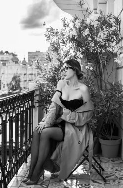 Bej ceketli, çoraplı ve siyah iç çamaşırlı bir kadın. Avrupalı sarışının balkondaki şehvetli fotoğrafı..