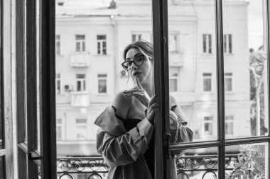 Bej ceketli, çoraplı ve siyah iç çamaşırlı bir kadın. Avrupalı sarışının balkondaki şehvetli fotoğrafı..