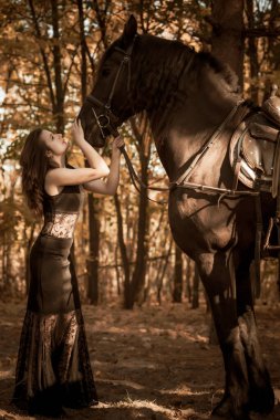 Kadınlık kavramı. Siyah elbiseli genç bir kadın ve bir at. Siyah atlı güzel kız.