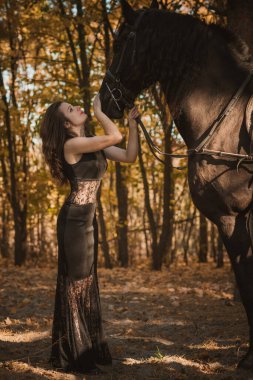 Kadınlık kavramı. Siyah elbiseli genç bir kadın ve bir at. Siyah atlı güzel kız.