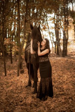 Kadınlık kavramı. Siyah elbiseli genç bir kadın ve bir at. Siyah atlı güzel kız.