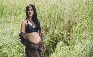 Uzun saçlı çingene kız doğaya poz veriyor. İnce vücutlu, atletik vücutlu, örgü kazaklı, seksi bir hırka giymiş, klasik bir kadın.