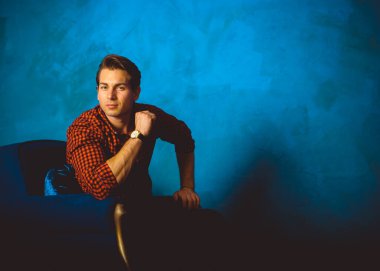 Yakışıklı genç adam. Ekose gömlekli şık bir adam mavi iç planda oturuyor. Güzel erkek model. 