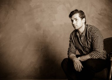 Yakışıklı genç adam. Ekose gömlekli şık bir adam mavi iç planda oturuyor. Güzel erkek model. 