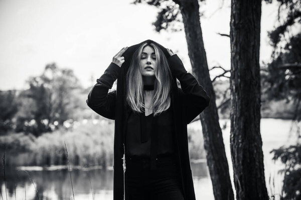 Элегантная светло-серая ведьма в капюшоне, идущая по таинственному лесу