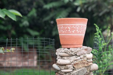 Rustic Clay Pot on the block of stones in Nature near the metal net fence - Earthy Outdoor Setting clipart