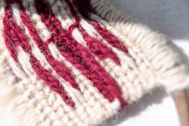 Gürcistan bayrağının tasarımını içeren bir makrome duvar örülmüş kumaşın dokusunu ve tersten işçiliğini vurguluyor.