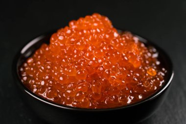 Siyah arka plan üzerinde siyah bir kasede kırmızı havyar, yakın çekim.