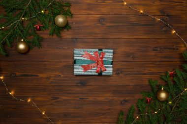 Noel hediyesi kutusu, köknar dalları ve çelenklerle çerçevelenmiş koyu ahşap bir arka planda..