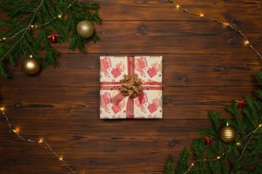 Noel hediyesi kutusu, köknar dalları ve çelenklerle çerçevelenmiş koyu ahşap bir arka planda..