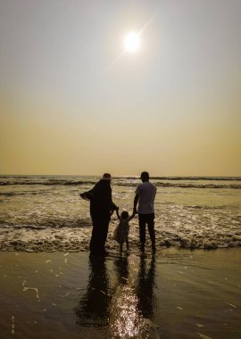 Aile Yürüyüşü Sahil Günbatımı Seyahat Tatil Konsepti. Ebeveynler ve kızları aktif bir aile tatilinde sahilde yürüyorlar..
