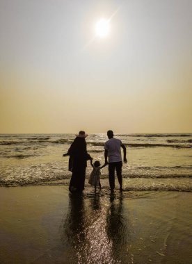 Aile Yürüyüşü Sahil Günbatımı Seyahat Tatil Konsepti. Ebeveynler ve kızları aktif bir aile tatilinde sahilde yürüyorlar..