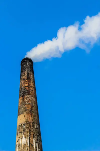 The chimney of brick field emitting heavy smoke with unhealthy carbon di oxide responsible for damaging ozone layer. Factory smoke causes pollution in the air. Fuming chimney against blue sky.