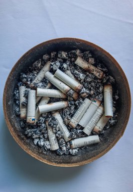 Kötü bağımlılık. Kül tablası ve sigaralar yakın plan. Masadaki kül tablasının yakın görüntüsü. Bir sürü yanmış sigara izmariti ve biraz da kül. Kül tablasında yanan sigaranın tepesinde.