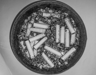 Kötü bağımlılık. Kül tablası ve sigaralar yakın plan. Masadaki kül tablasının yakın görüntüsü. Bir sürü yanmış sigara izmariti ve biraz da kül. Kül tablasında yanan sigaranın tepesinde.