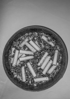 Kötü bağımlılık. Kül tablası ve sigaralar yakın plan. Masadaki kül tablasının yakın görüntüsü. Bir sürü yanmış sigara izmariti ve biraz da kül. Kül tablasında yanan sigaranın tepesinde.